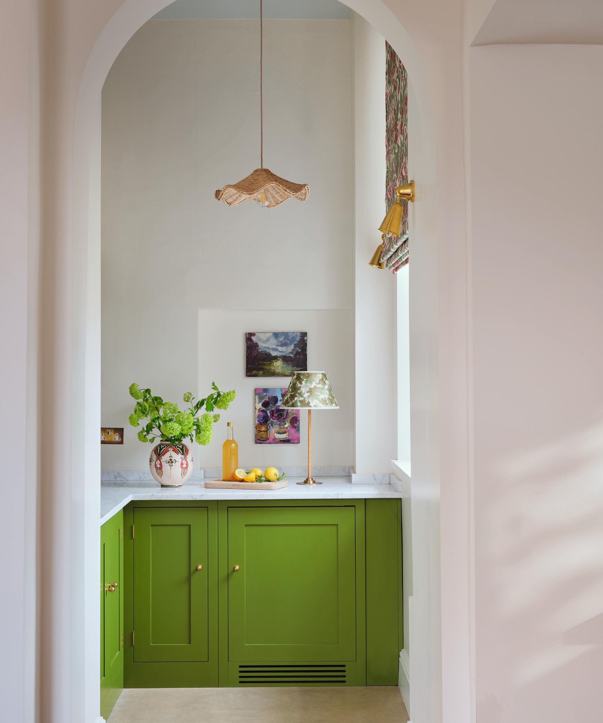 an arched doorway into a bright green painted pantry with marble counters and a rattan wavy pendant