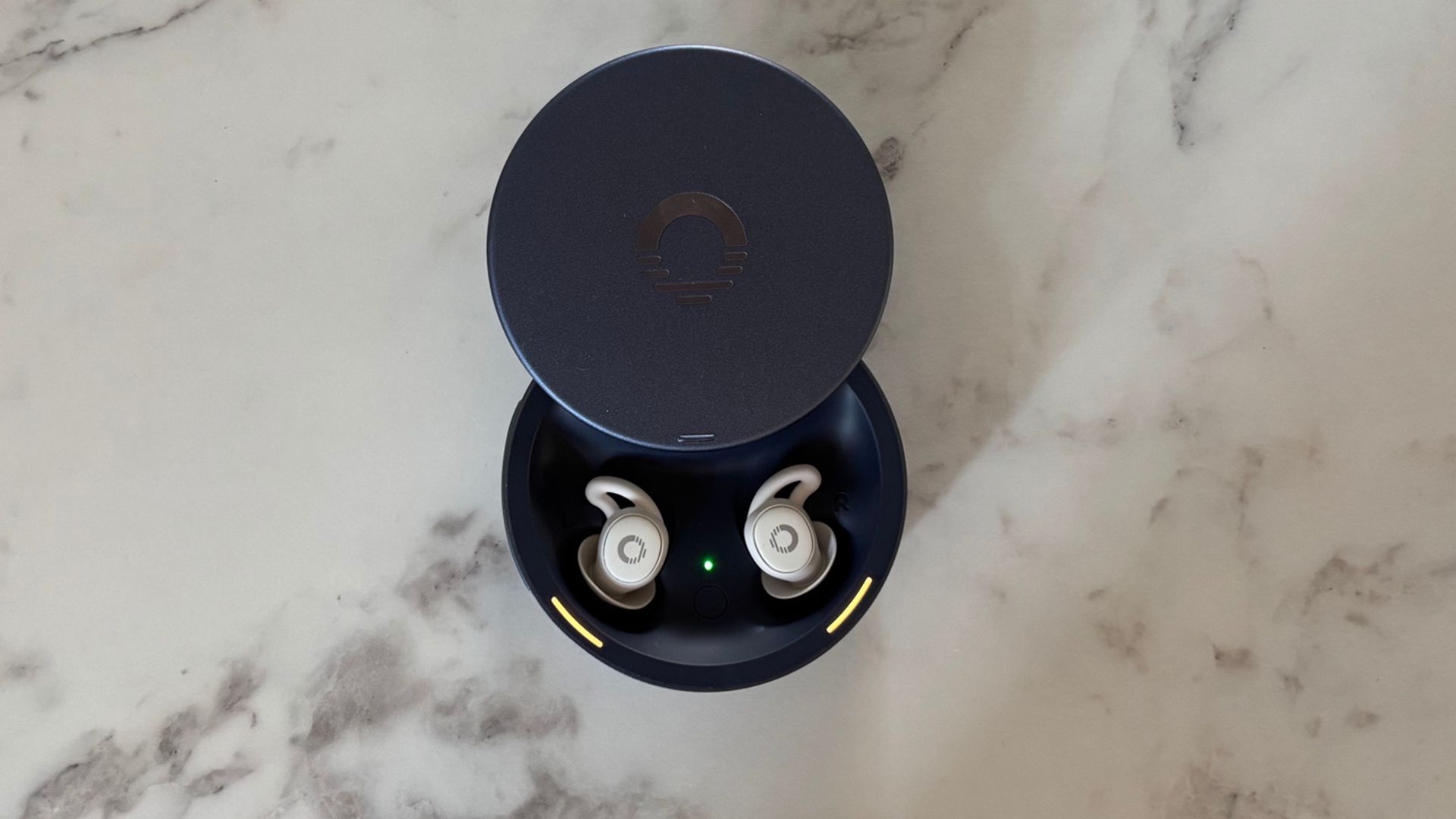 Image shows the white Ozlo Sleepbuds 2 in their battleship blue circular case, placed on a marble counter