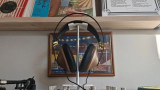 Meze Audio 99 Classics 2nd Gen wired headphones, on a headphone stand, in front of a bookshelf and framed picture.