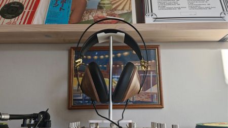Meze Audio 99 Classics 2nd Gen wired headphones, on a headphone stand, in front of a bookshelf and framed picture.