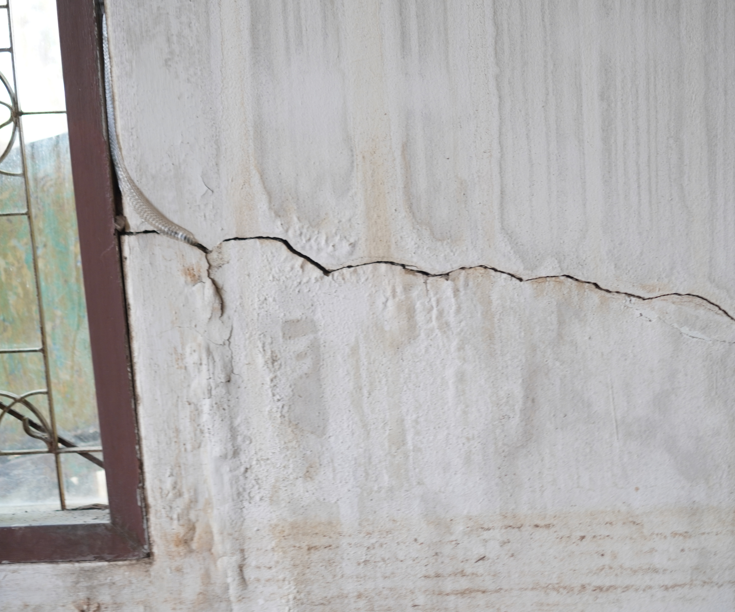 white wall with large crack leading to brown window frame