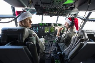 Two men in army uniforms and Santa hats while flying a plane