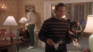 Chevy Chase in a sweater carrying two egg nog glasses