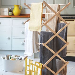 Wooden clothes airer with clothes on in a kitchen with a bucket of cleaning products next to it