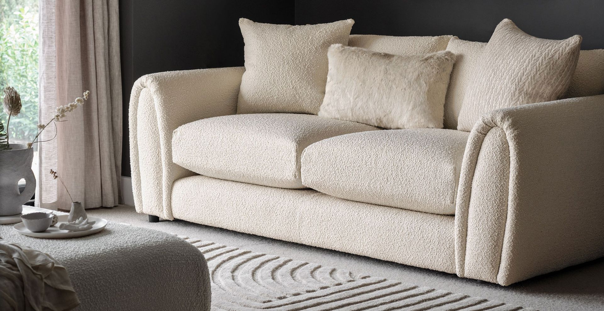 black living room with cream boucle sofa with matching cream rug showing a key material for sofa trends 2023