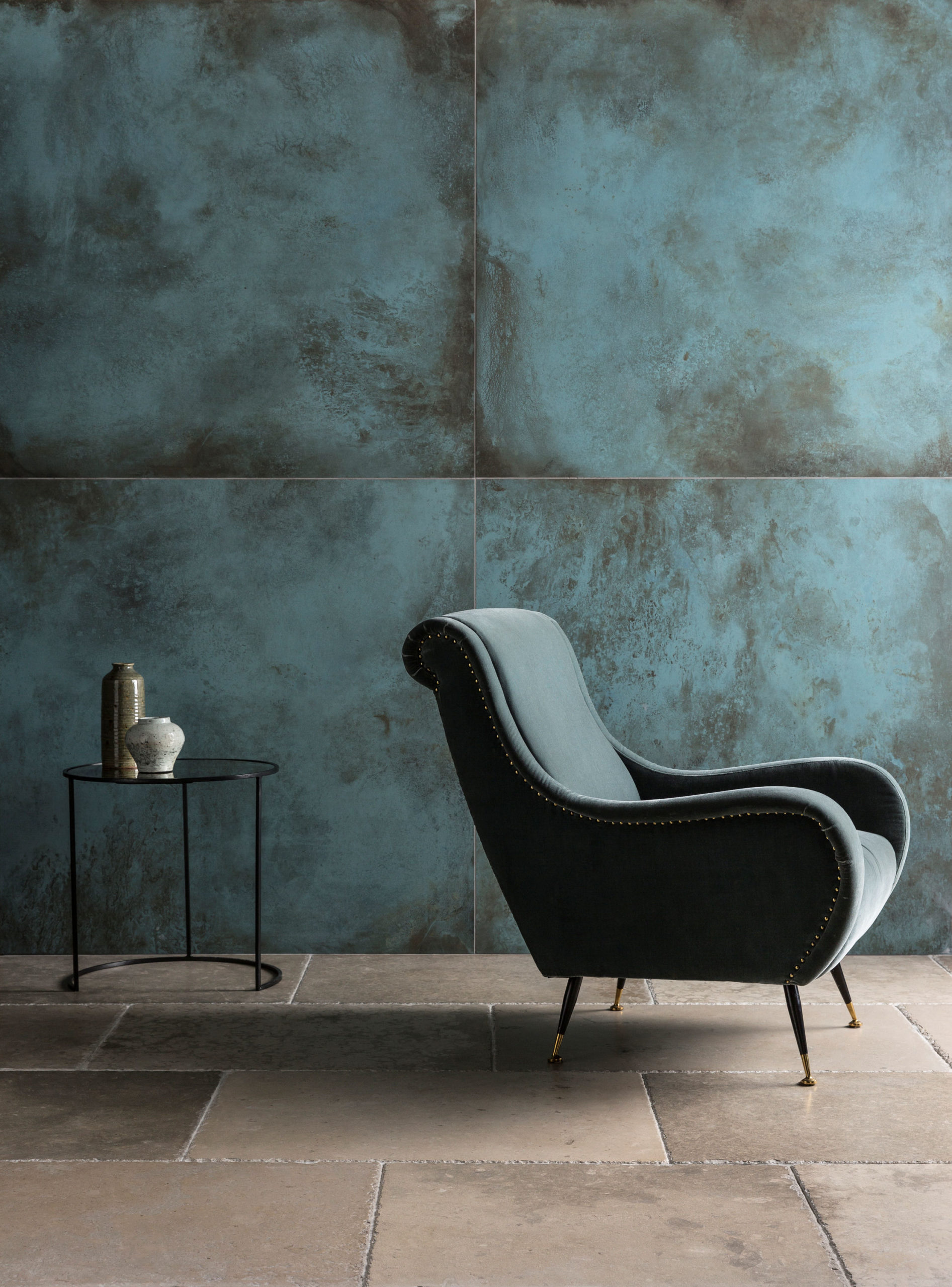 Large dark blue-grey wall tiles behind a grey armchair.