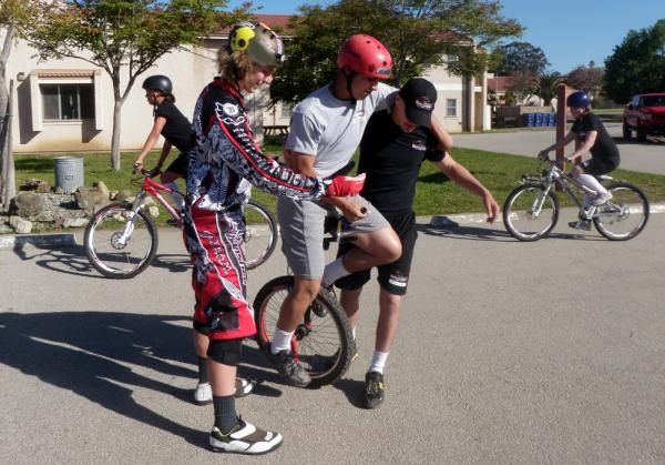 A young rider gets some assistance while learning to ride a unicycle.