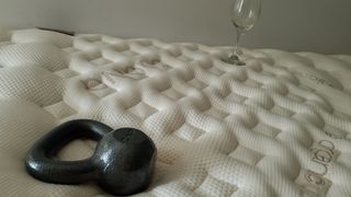 Saatva RX mattress review image shows a black weight and a wine glass placed on the mattress during testing the motion isolation with an empty wine glass and a 10lb weight
