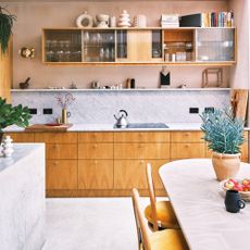 kitchen with wooden cabinets and shelving, light pink walls and dining table 
