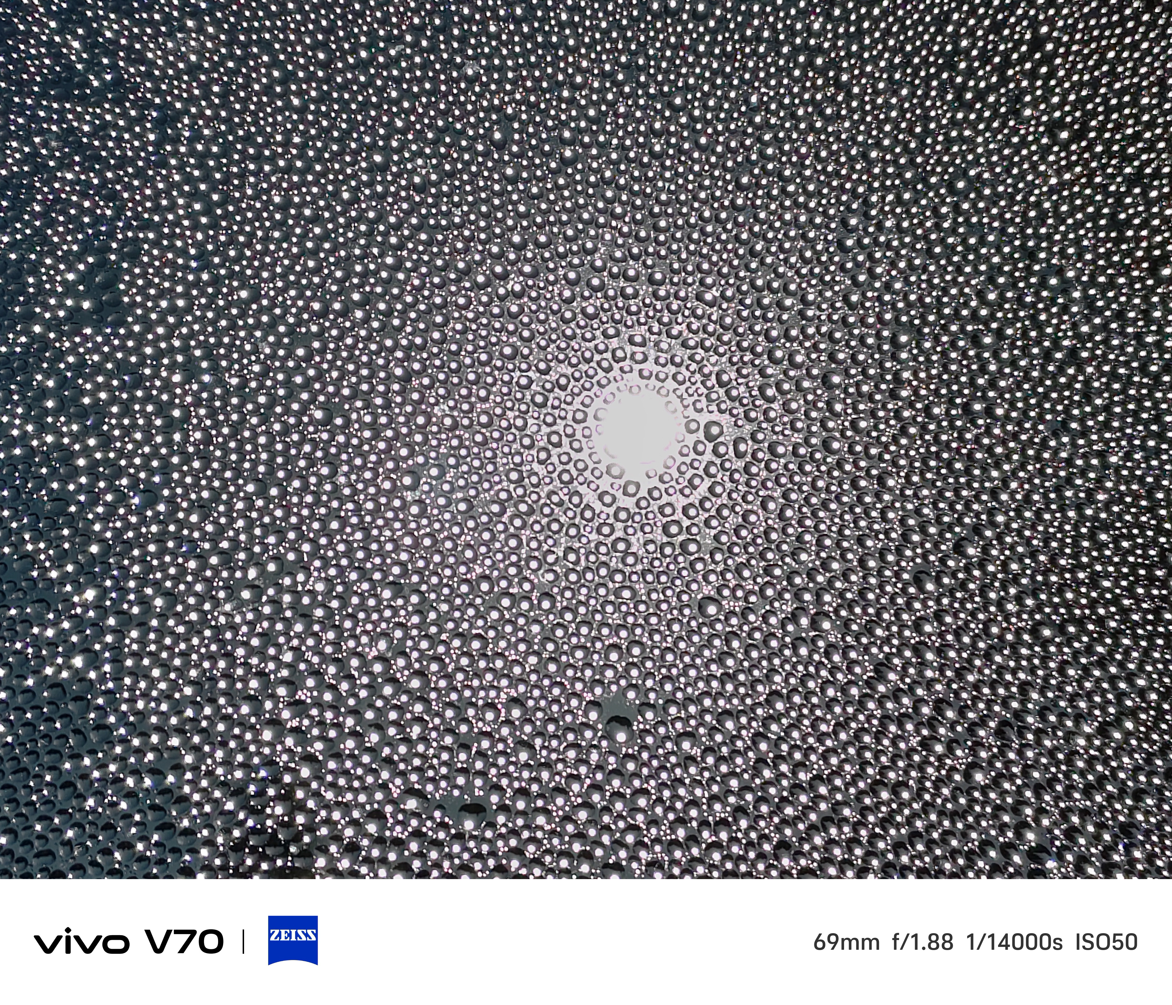 Abstract pattern of water droplets on glass radiating around a bright central light source.