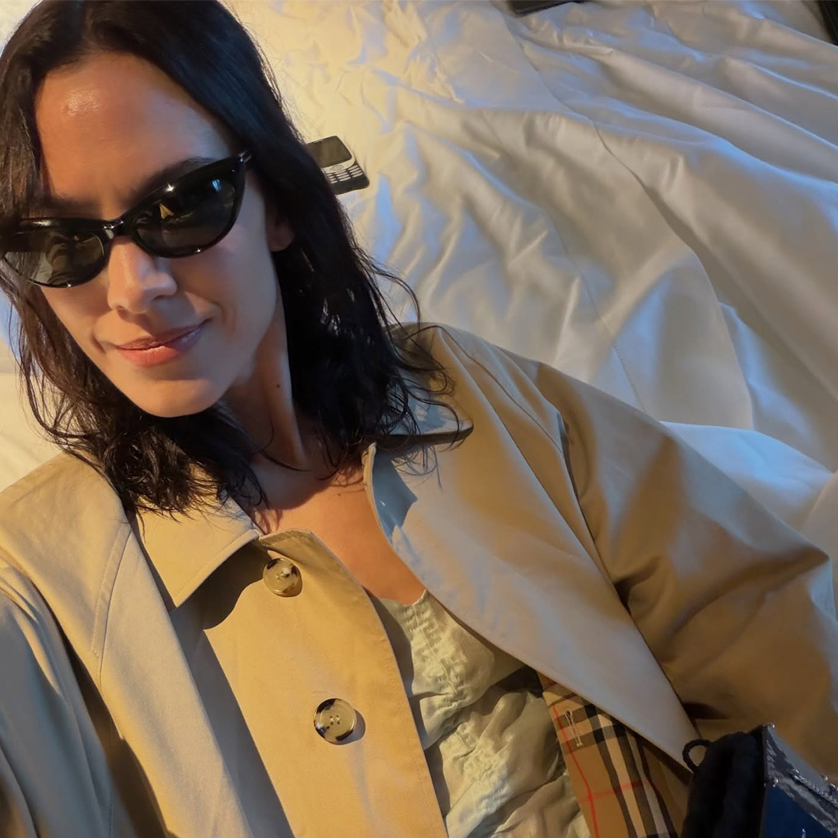 Alexa wears a trench coat and a ruched top.