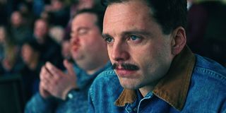 Sebastian Stan in I, Tonya with a denim jacket on watching ice skating with Paul Hauser in the background clapping.
