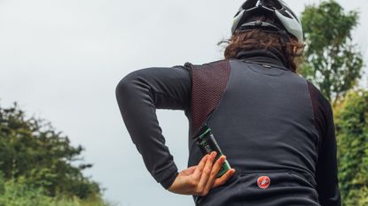 Female cyclist putting one of the best energy bars for cycling into her jersey back pocket on a bike ride
