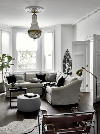 white living room with grey sectional couch, dark wooden floor, pouffe, black accents, bay window