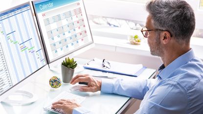 A businessman looks at a calendar on his computer screen while sitting at his desk at work.