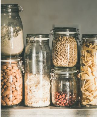An image of a set of glass storage jars with pasta, rice and nuts and seeds inside
