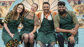 Lottie Bedlow, Manon Lagrève, Antony Amourdoux and Chigs Parmar in green aprons sit on stools in the tent for The Great British Bake Off New Year special.