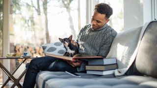 Man sitting on couch looking at books with Chihuahua on his lap