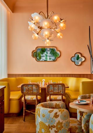 An Asian-style restaurant features apricot-shaded light and walls, yellow upholstered seating, and upholstered bamboo chairs matching the location's wooden tables.