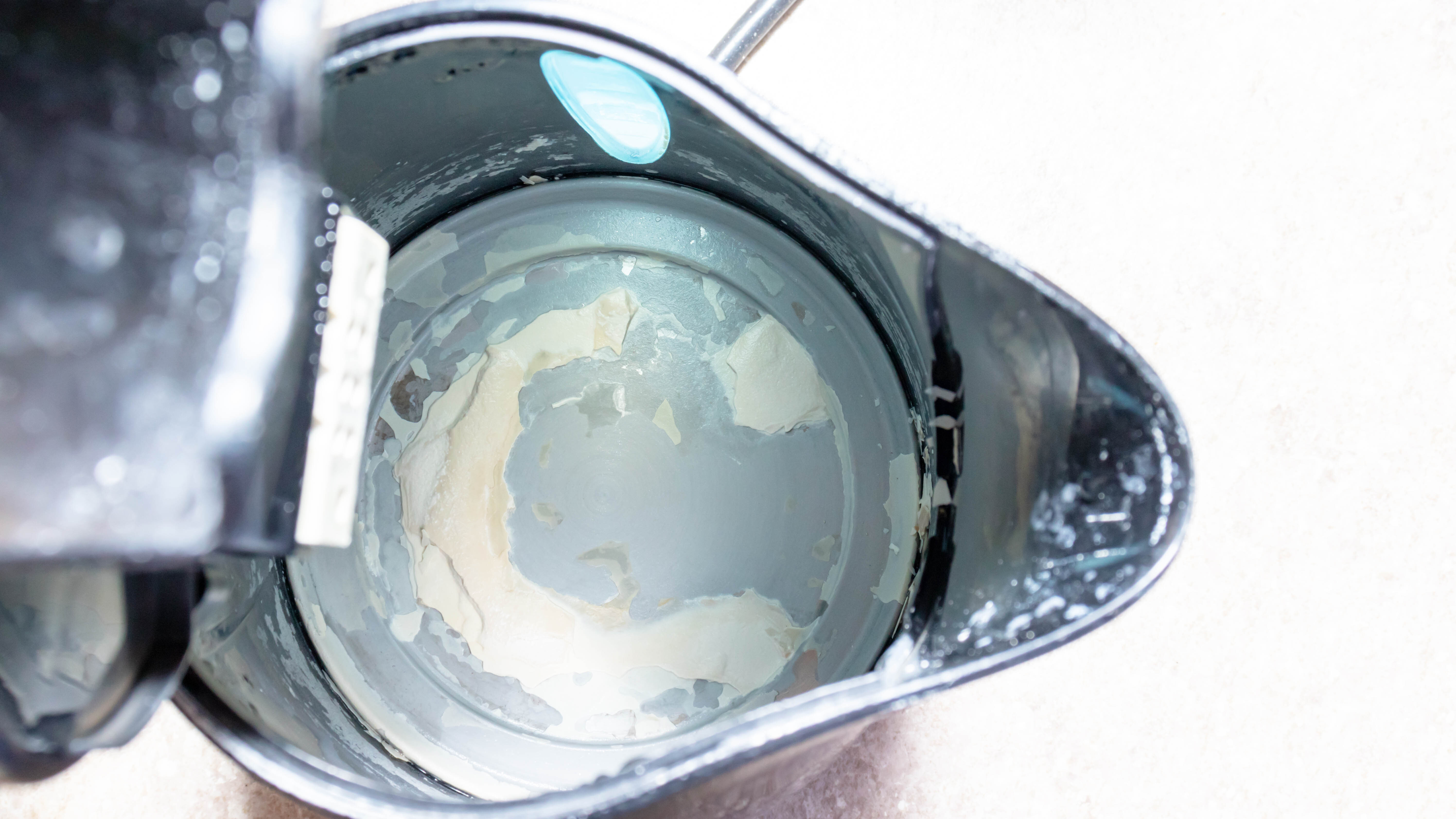 Вид изнутри чайника, наполовину наполненного водой, с скоплением накипи внутри.