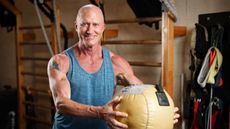Man in gym smiling at camera holding medicine ball