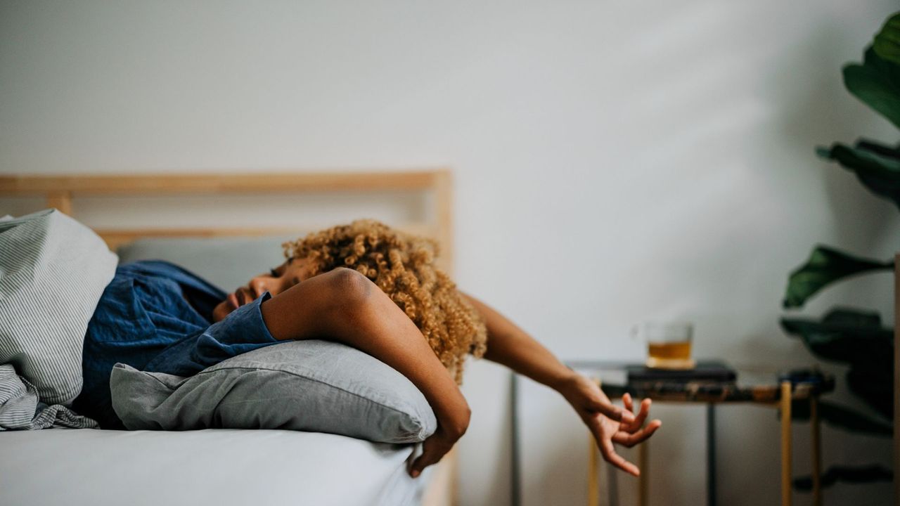 Woman lying backwards on bed, hands over head, representing how to sleep better