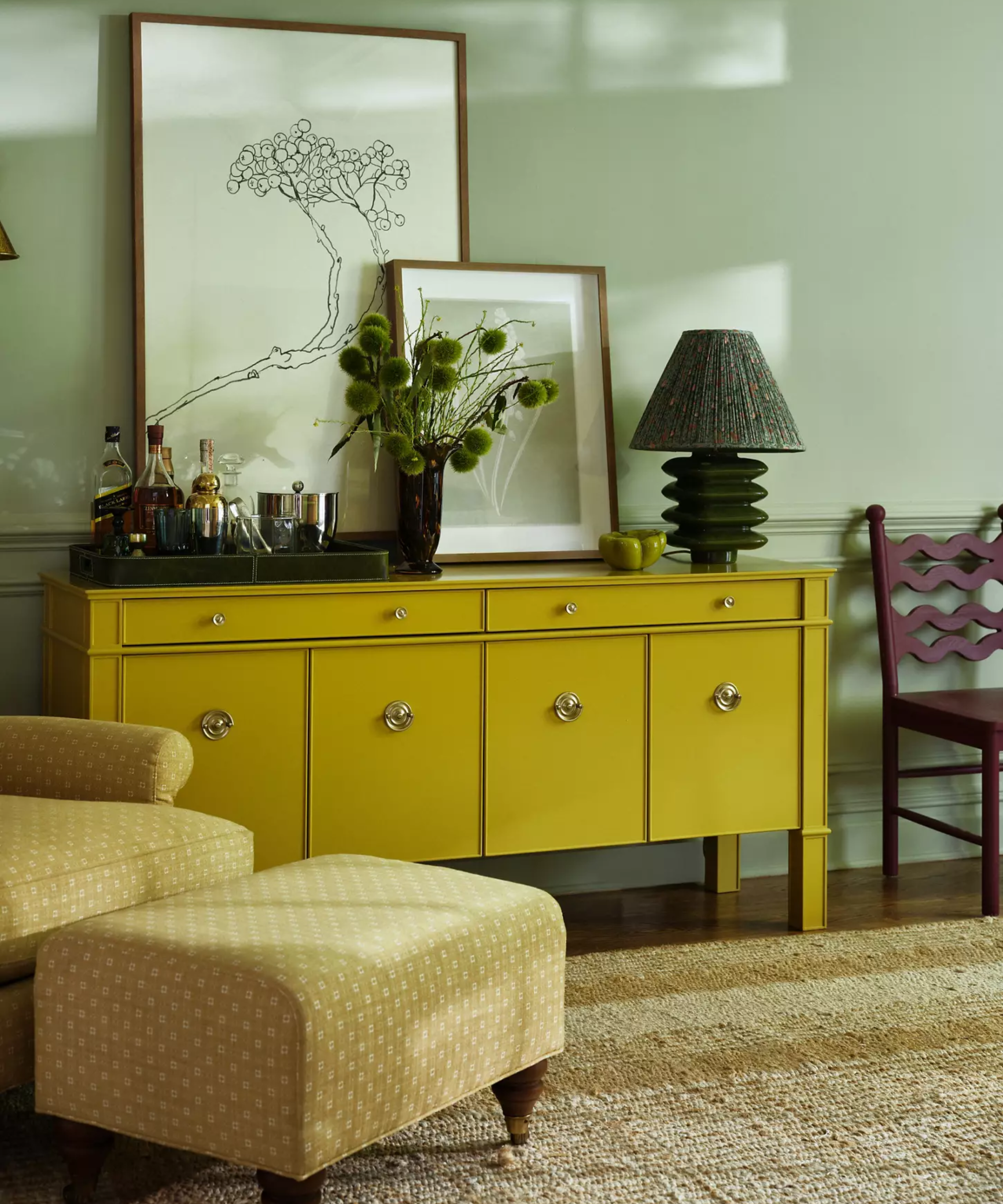 a room with green painted walls and a yellow credenza with gold handles on each of the doors