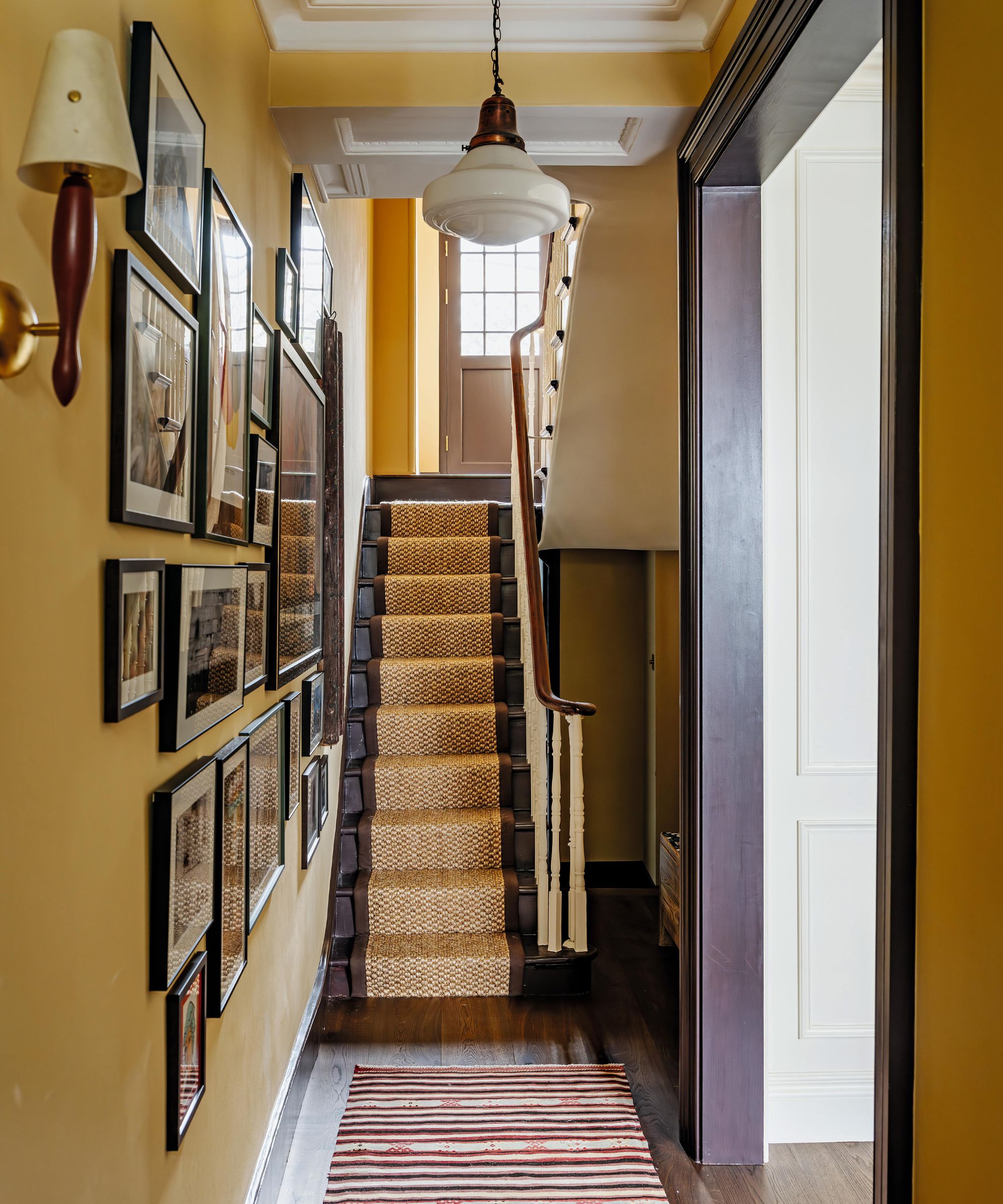 a bright yellow narrow hallway in a london townhouse with chocolate brown stairs and a gallery wall