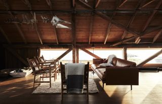 A Norwegian mountain retreat is captured at dusk, its woody loft filled with leather mid-century modern furniture, soft rugs, and a floating skeleton of a shark.