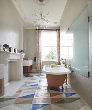 A bathroom with pink walls and freestanding bath, contemporary chandelier and tiled floors