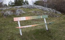 A park bench is painted to look like a color palette. It goes from peach tones to green.