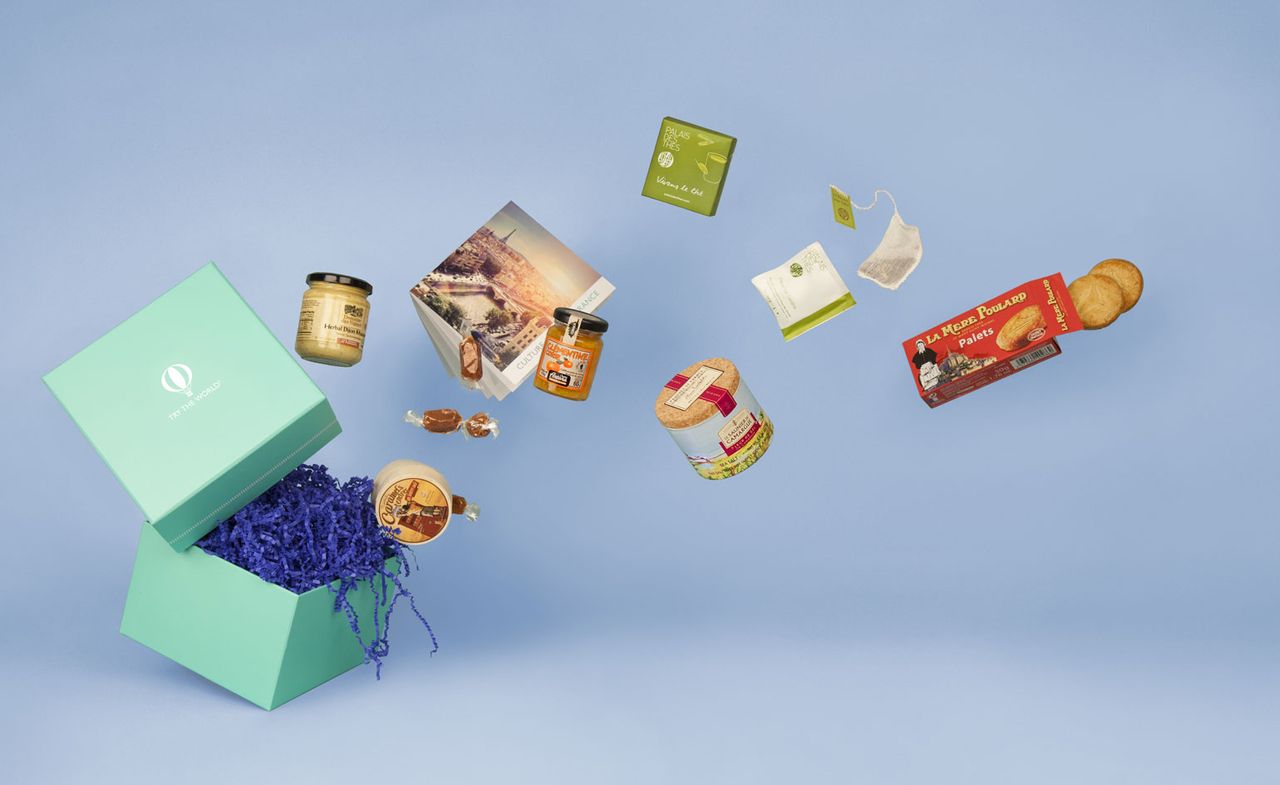 A photo of Try The World box with its contents of it &#039;flying out. Photographed on a blue background.