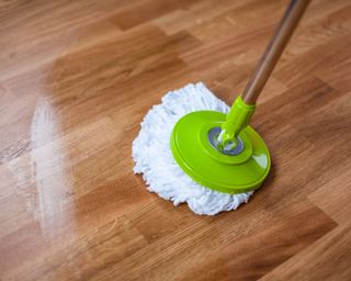 A green mop cleaning wooden flooring.