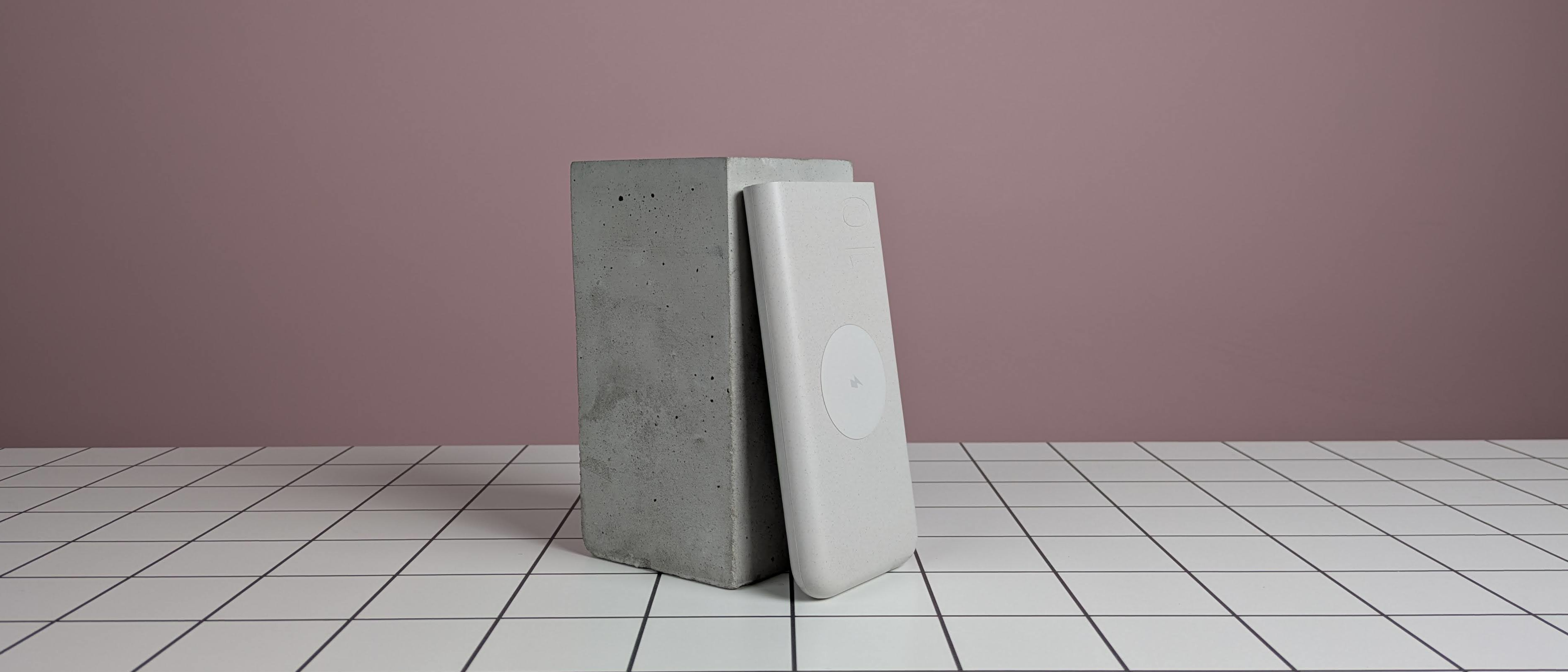 Samsung 25W 10,000mAh Wireless Battery Pack leaning on plinth, on desk with pink background