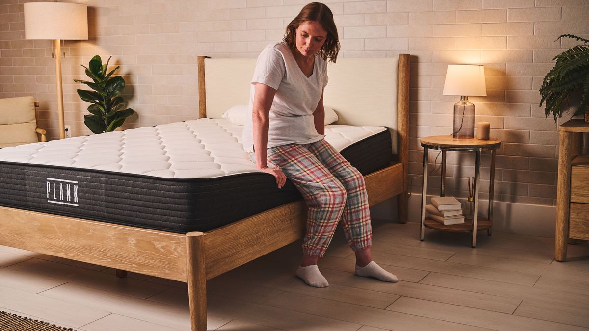 A person sits on the edge of the Plank Firm mattress, Extra Firm side, to test the edge support