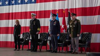 four people, three of whom are in u.s. military uniforms, stand in front of an American flag
