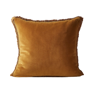 An ochre velvet throw pillow with fringed edge
