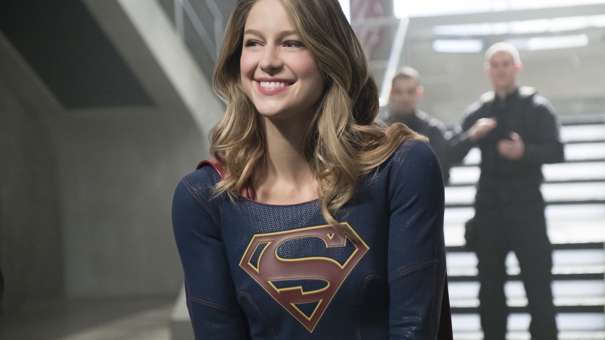 Still from the Supergirl TV series. A happy Supergirl being applauded.