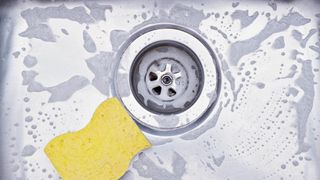 Sink drainer and yellow sponge with soap suds surrounding