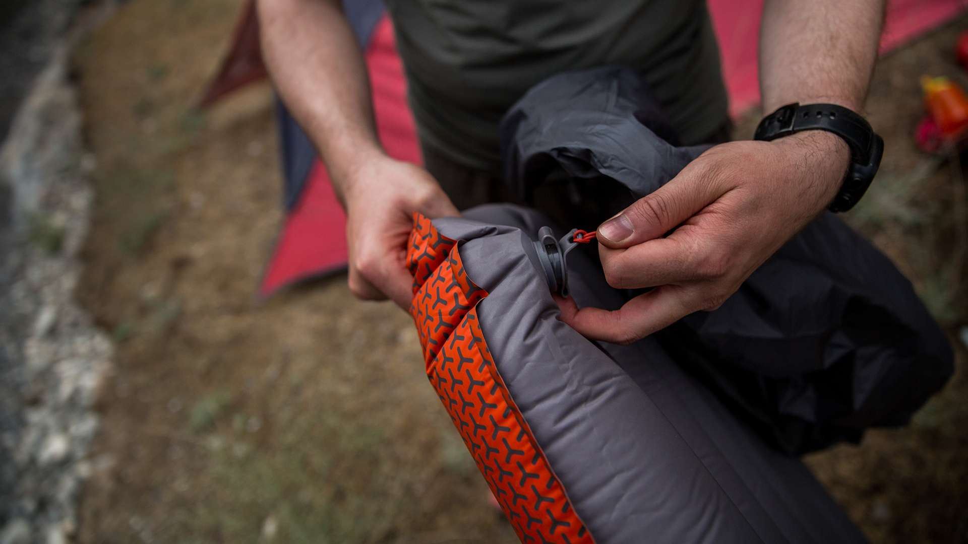 Hands hold a Rab Ionosphere 5.5 Sleep Mat, pulling the popper out to deflate.
