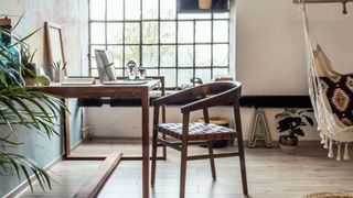 Stylish interior design of office space in loft apartment with wooden desk, chair, office supplies, laptop, plants, hammock and elegant accessories.