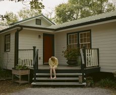 film still from kinds of kindness showing emma stone in front of timber house