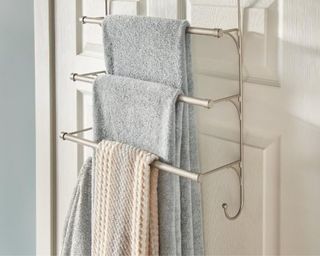 A bathroom door towel rack with several towels on a white door and grey walls in the background