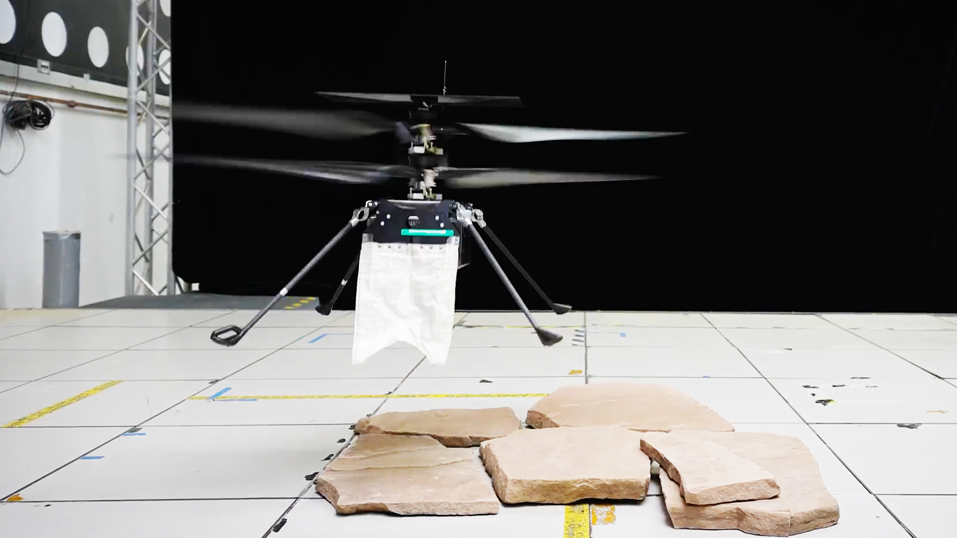 A tiny helicopter drone has a small white cape. 
