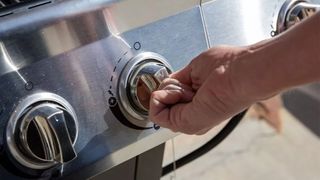 A hand turning one of the switches on the Nexgrill 5-Burner Propane Gas Grill