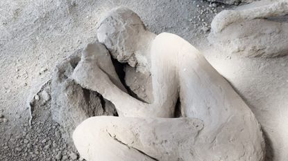 A close up of a white plaster cast of a person lying on the ground in a fetal position.
