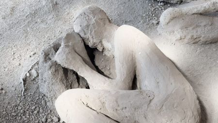 A close up of a white plaster cast of a person lying on the ground in a fetal position.