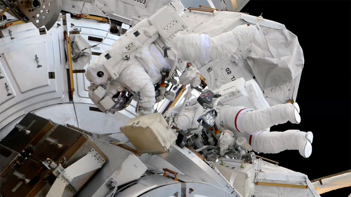 two astronauts in white spacesuits are seen outside a space station during a spacewalk