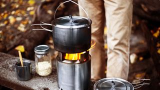 A pot on a camping stove with a camper in the background