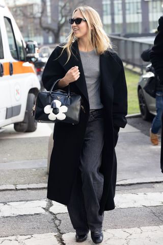 A photo of Lila Moss topping her look with a black coat and black boots.